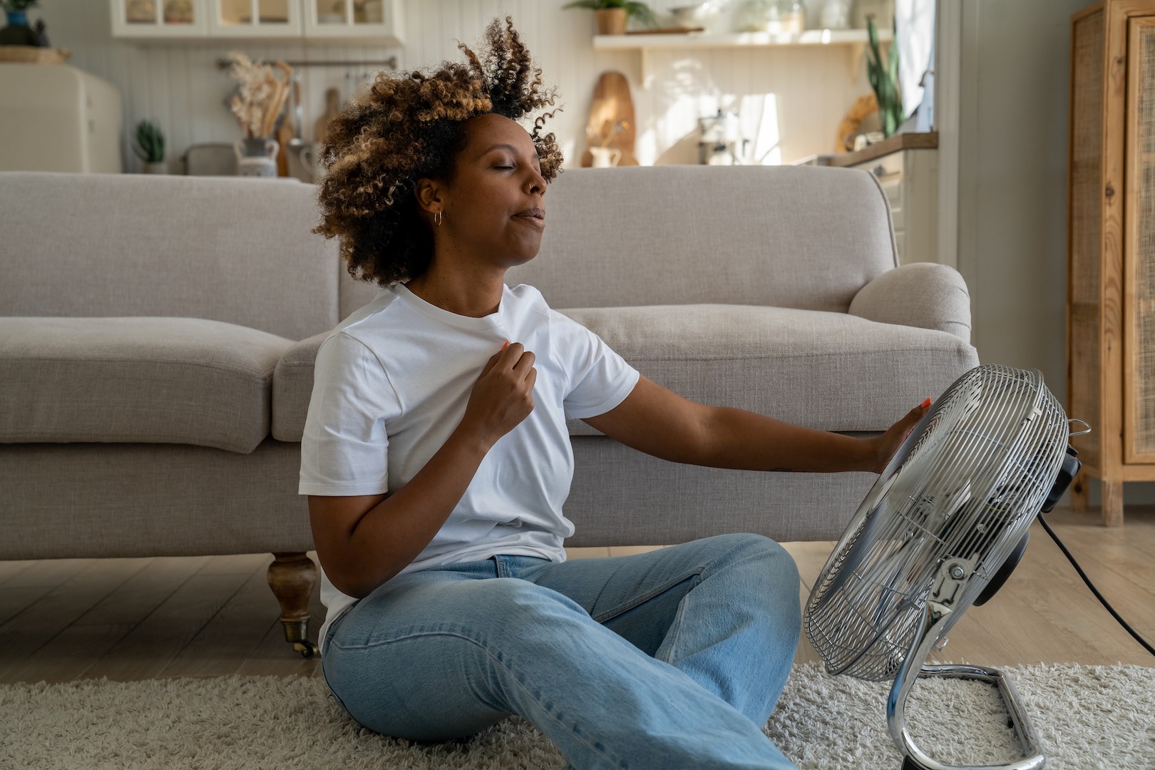 Woman sitting indoors sweating during a heatwave emphasizing the need for effective cooling solutions